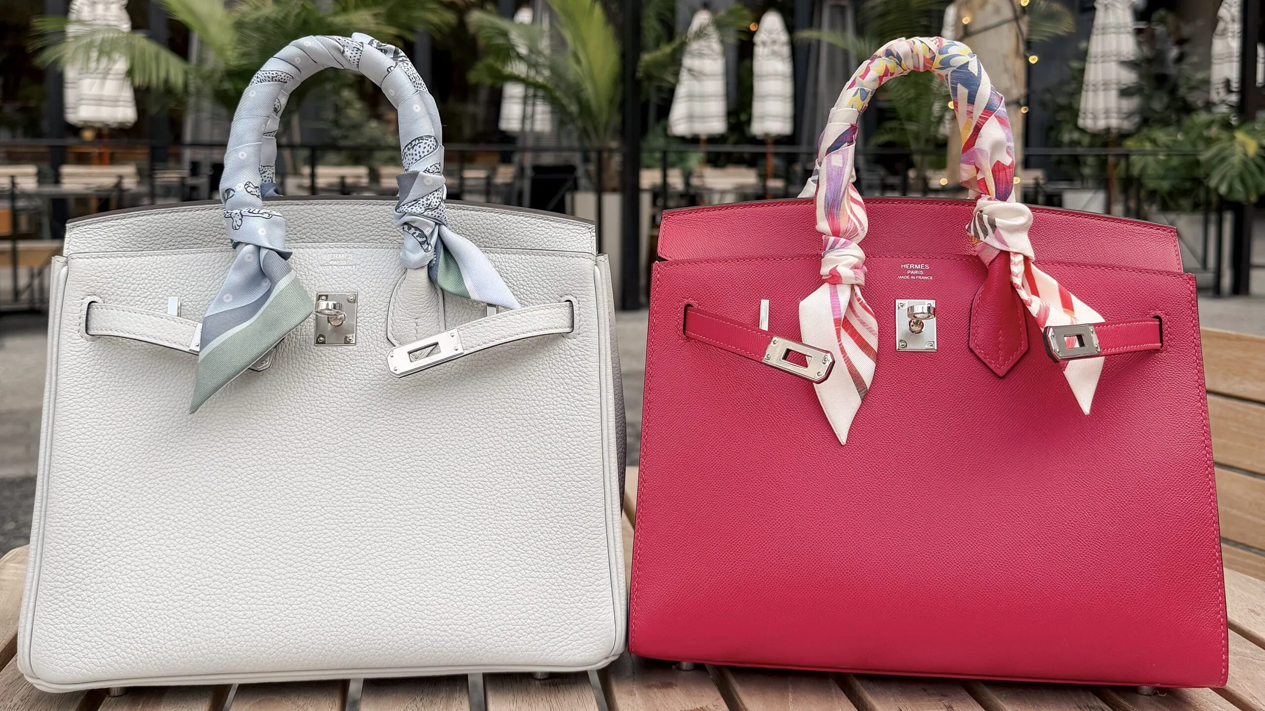 A white Togo Birkin Retourne and a rose Epsom Birkin Sellier side by side on an outdoor table