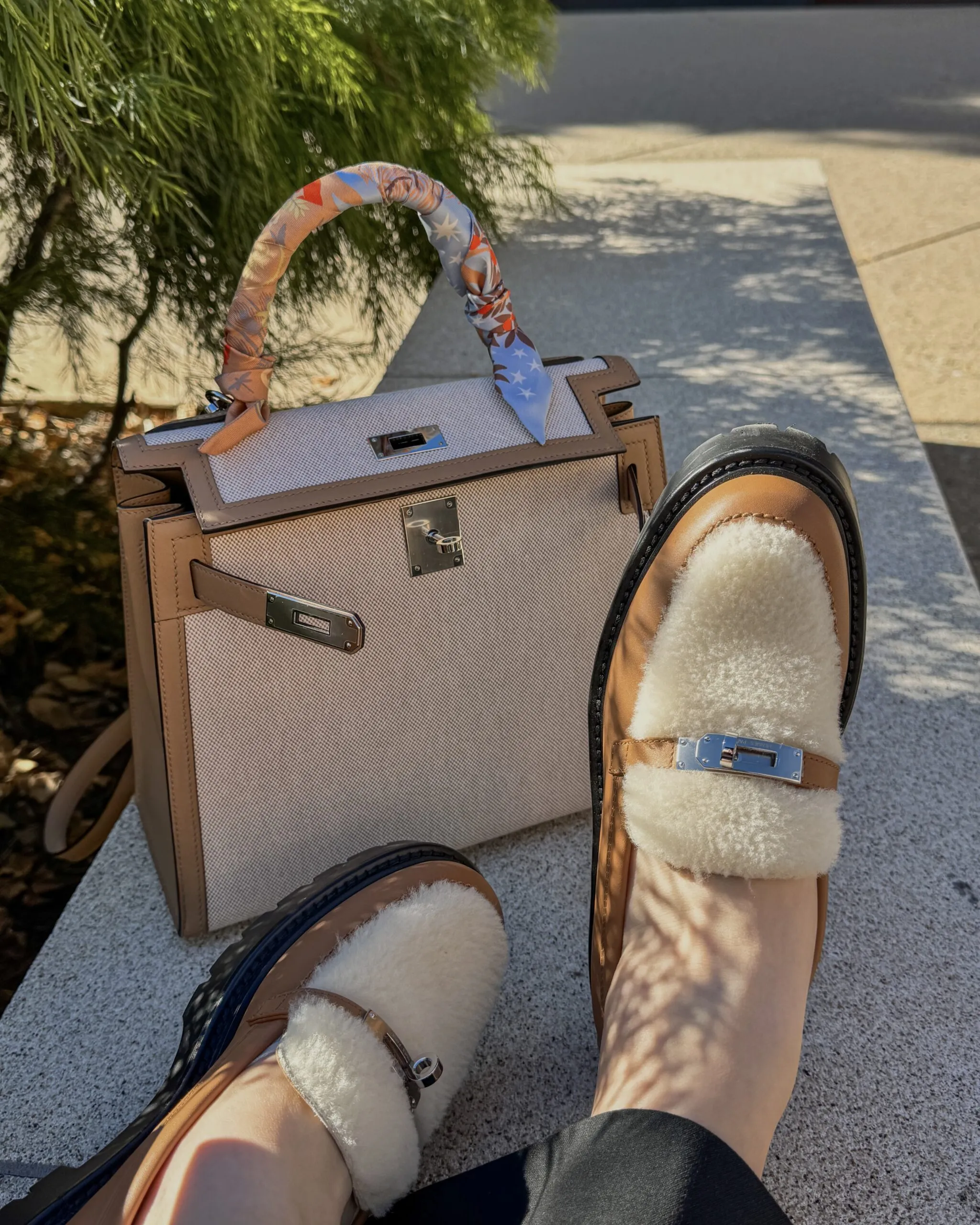 An Hermès Kelly in toile and tan leather beside shearling-lined loafers with Kelly-lock hardware