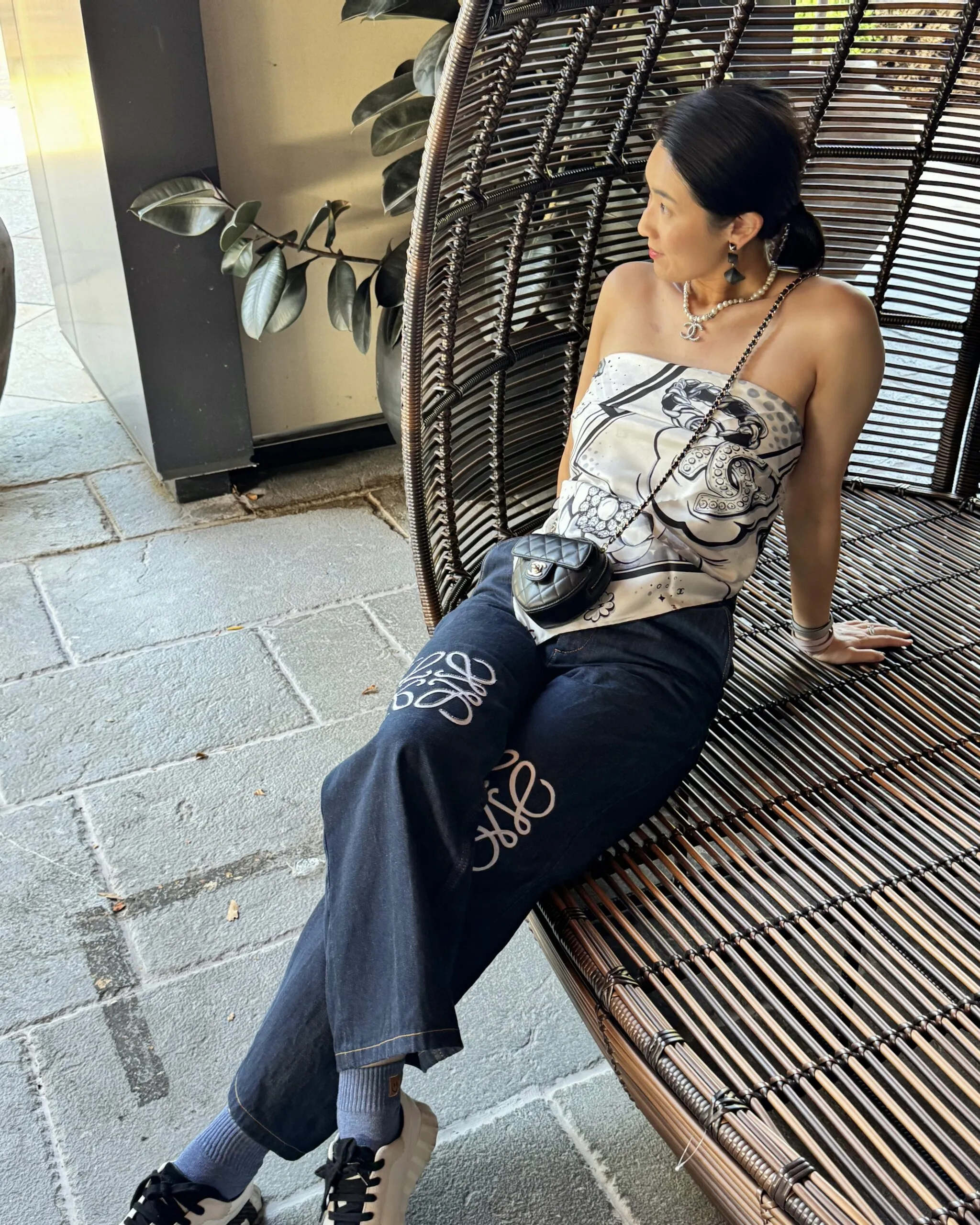 Lily in a Chanel silk scarf top and logo denim, relaxing in a woven hanging chair