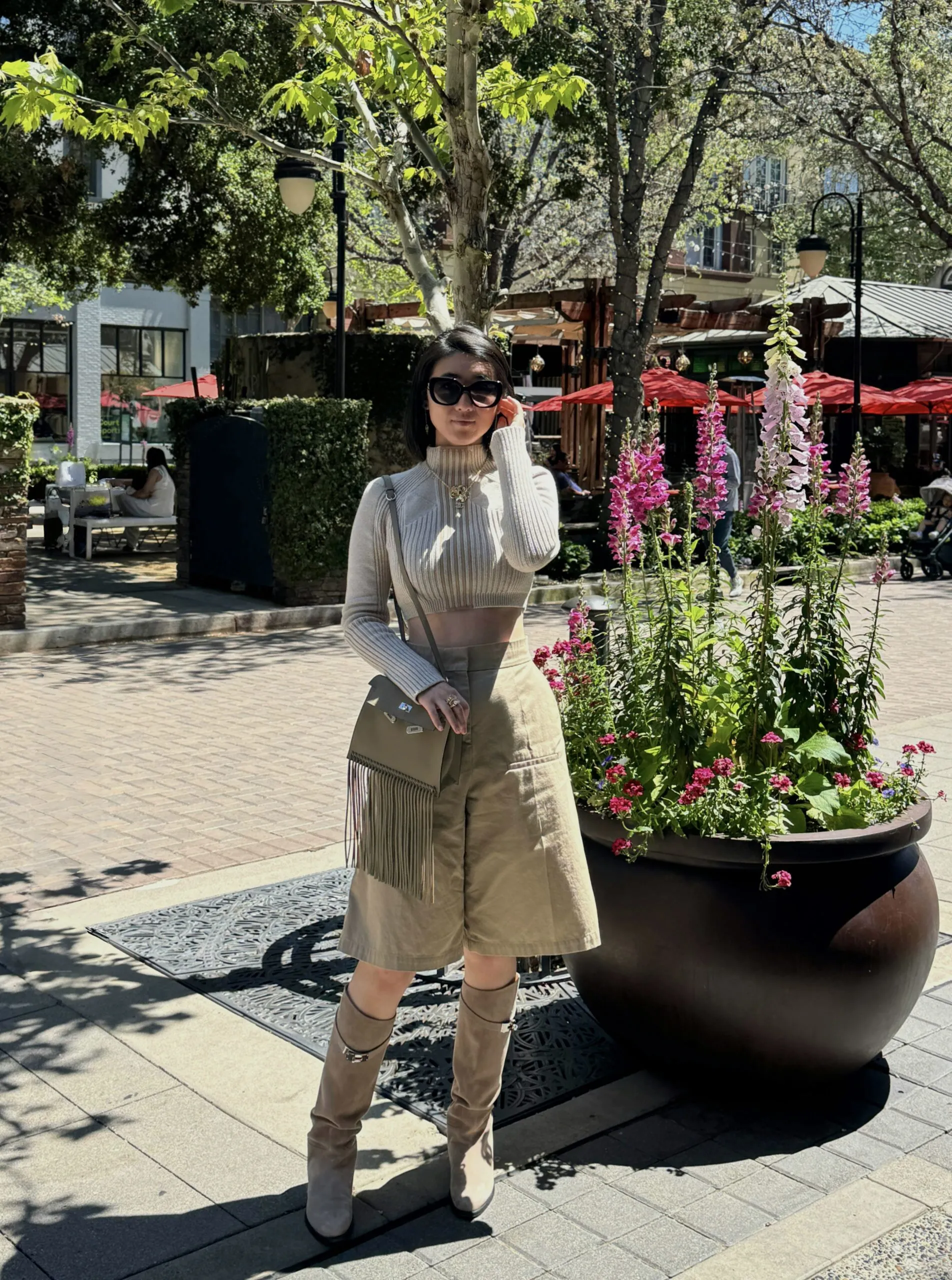 Lily outdoors in a ribbed knit top, tailored shorts and knee-high boots with a fringed shoulder bag
